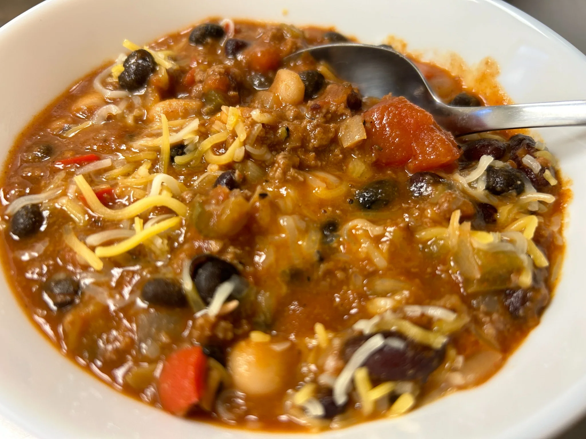 Bowl of chili bean soup with ground beef, black beans, peppers, tomatoes, and shredded cheese.