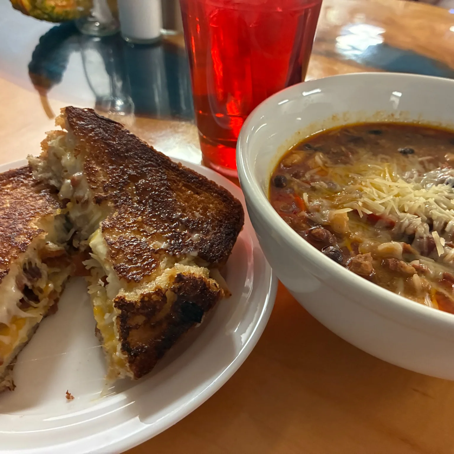 Grilled cheese sandwich served with a bowl of chili topped with shredded cheese.