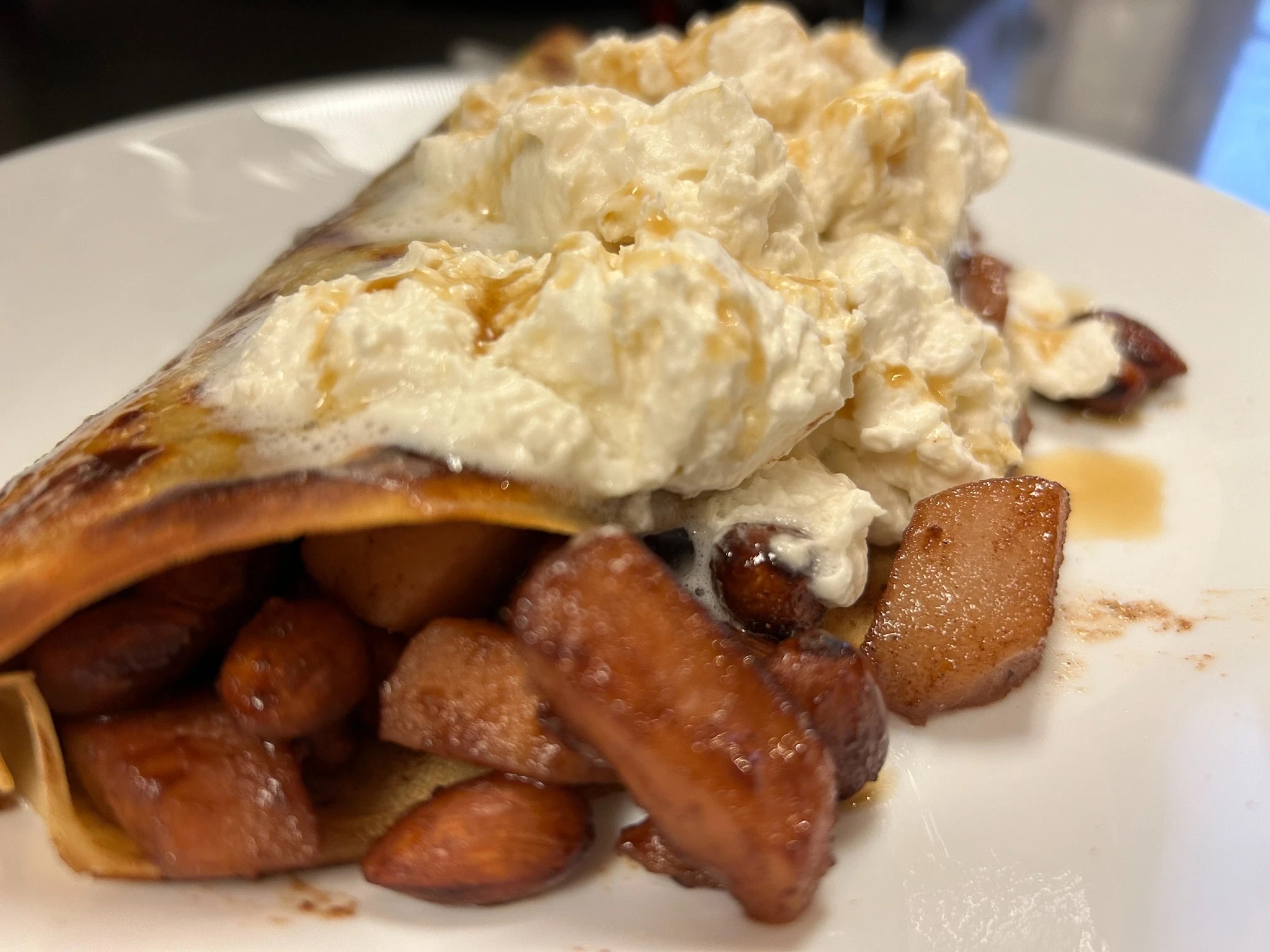 Ultra-thin crepe filled with caramelized pears, crunchy almonds, and topped with maple-infused whipped cream and syrup served on a white plate at Kat’s Café & Restaurant.