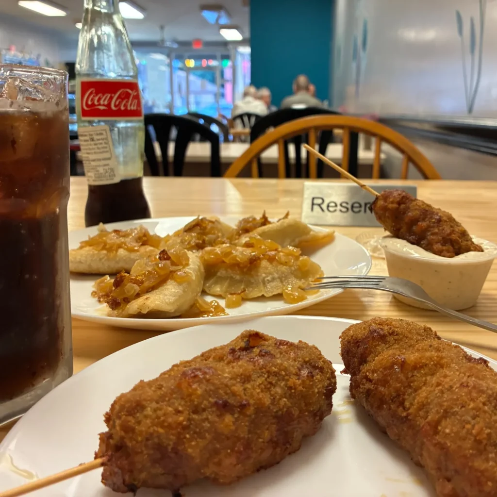 Breaded city chicken skewers and potato-cheese pierogies topped with sautéed onions on a table with iced cola and a glass bottle of Coca-Cola in Kat's dining room.