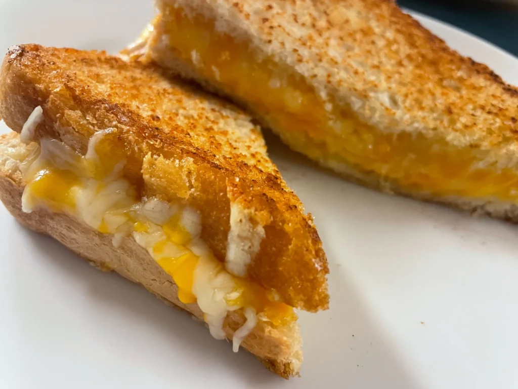 Buttery golden crisp toasted grilled cheese halves served on a white plate.