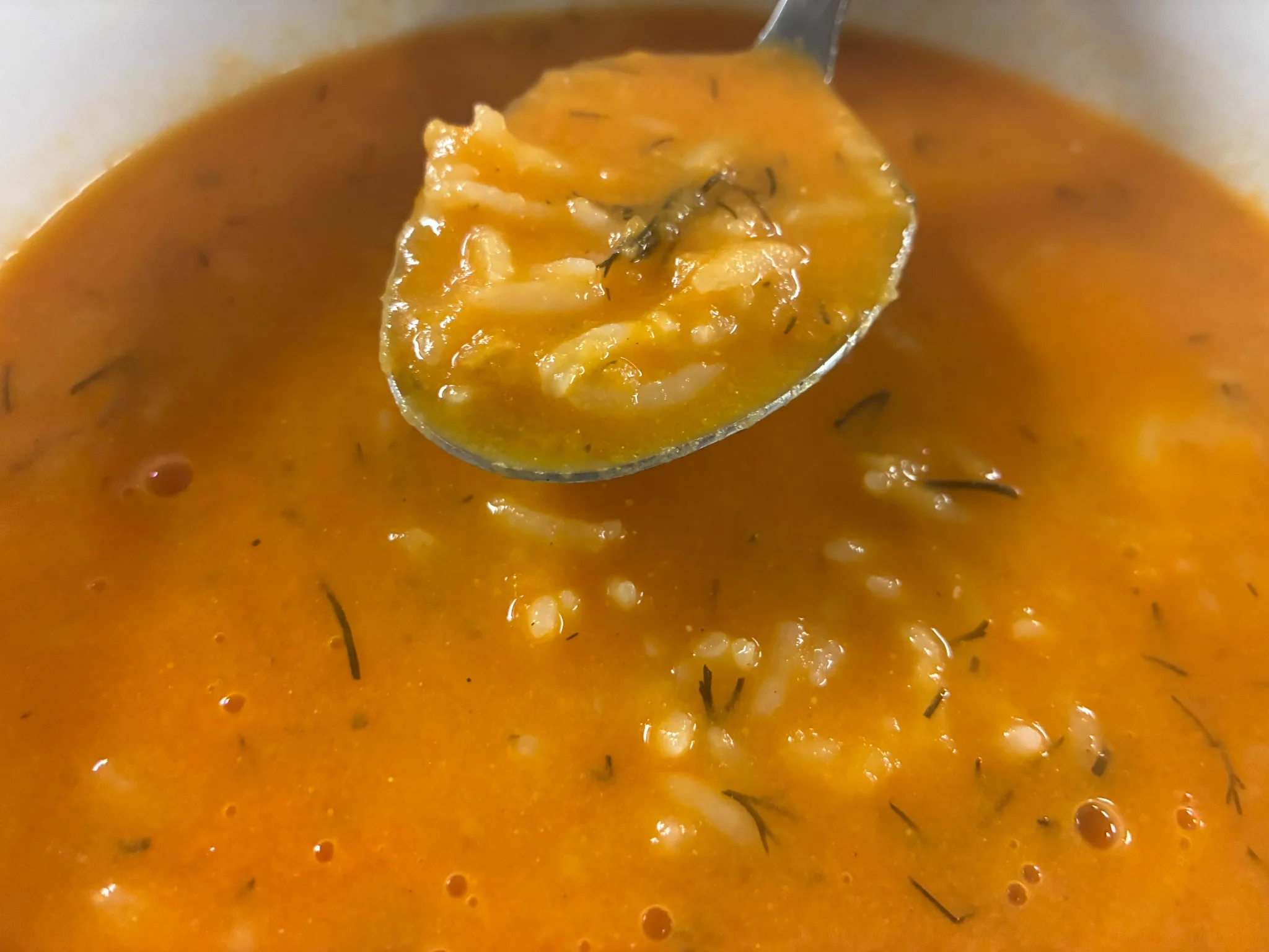 Creamy tomato soup with rice and herbs on a spoon above the bowl.