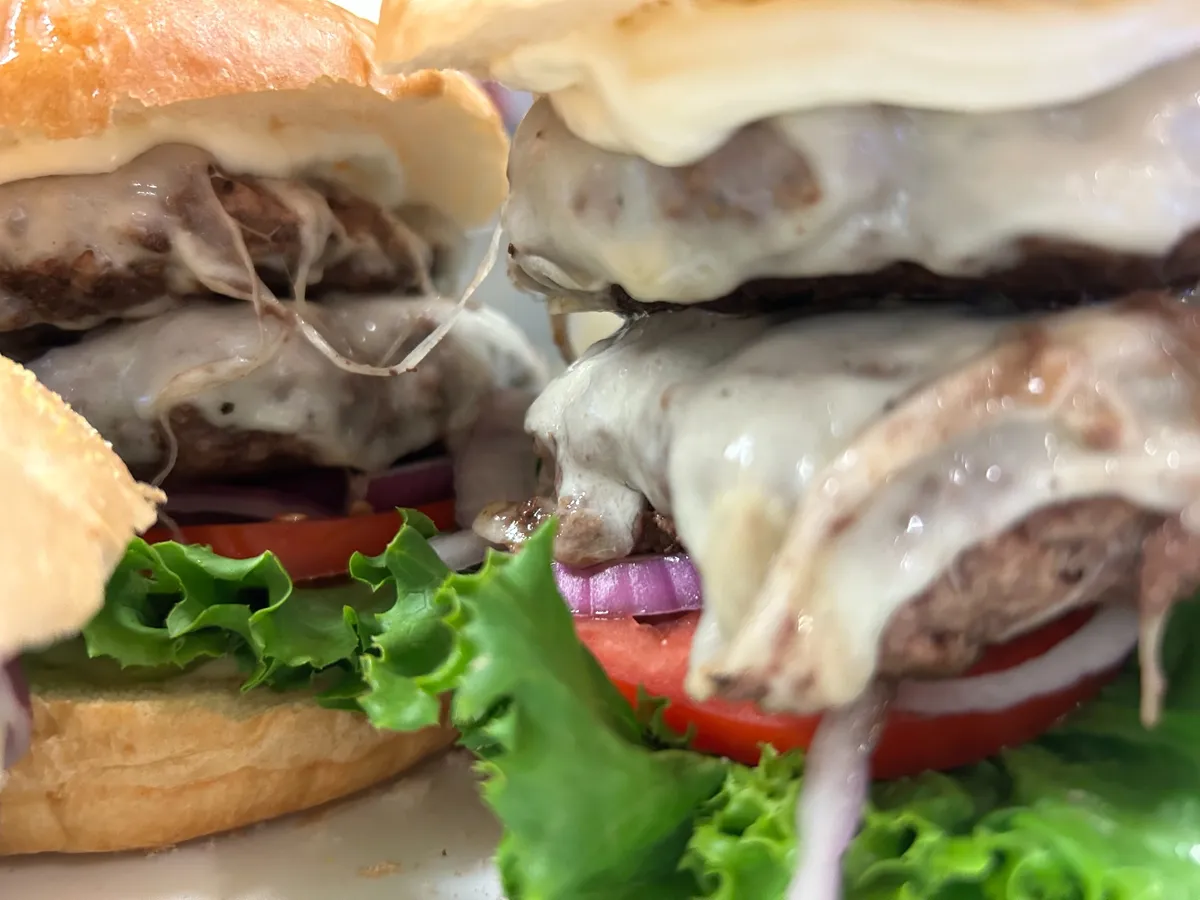 Close-up of multiple double smash burgers with melted cheese, lettuce, tomato and red onion.