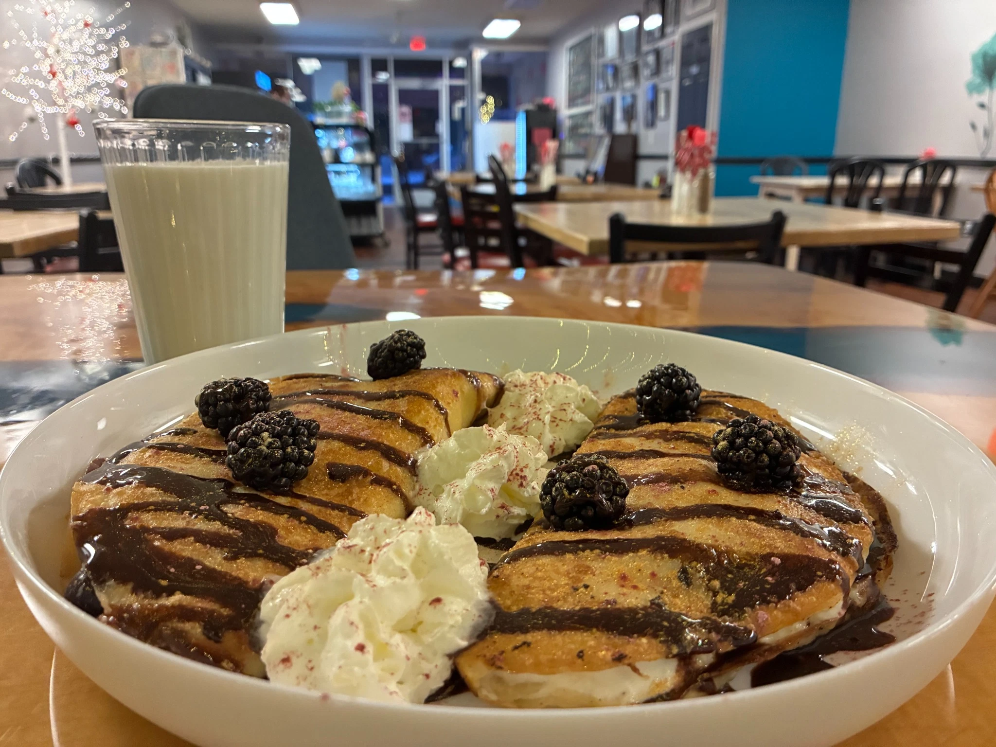 Double sweet cheese crepes in a bowl, finished with chocolate drizzle, whipped cream, and fresh blackberries.