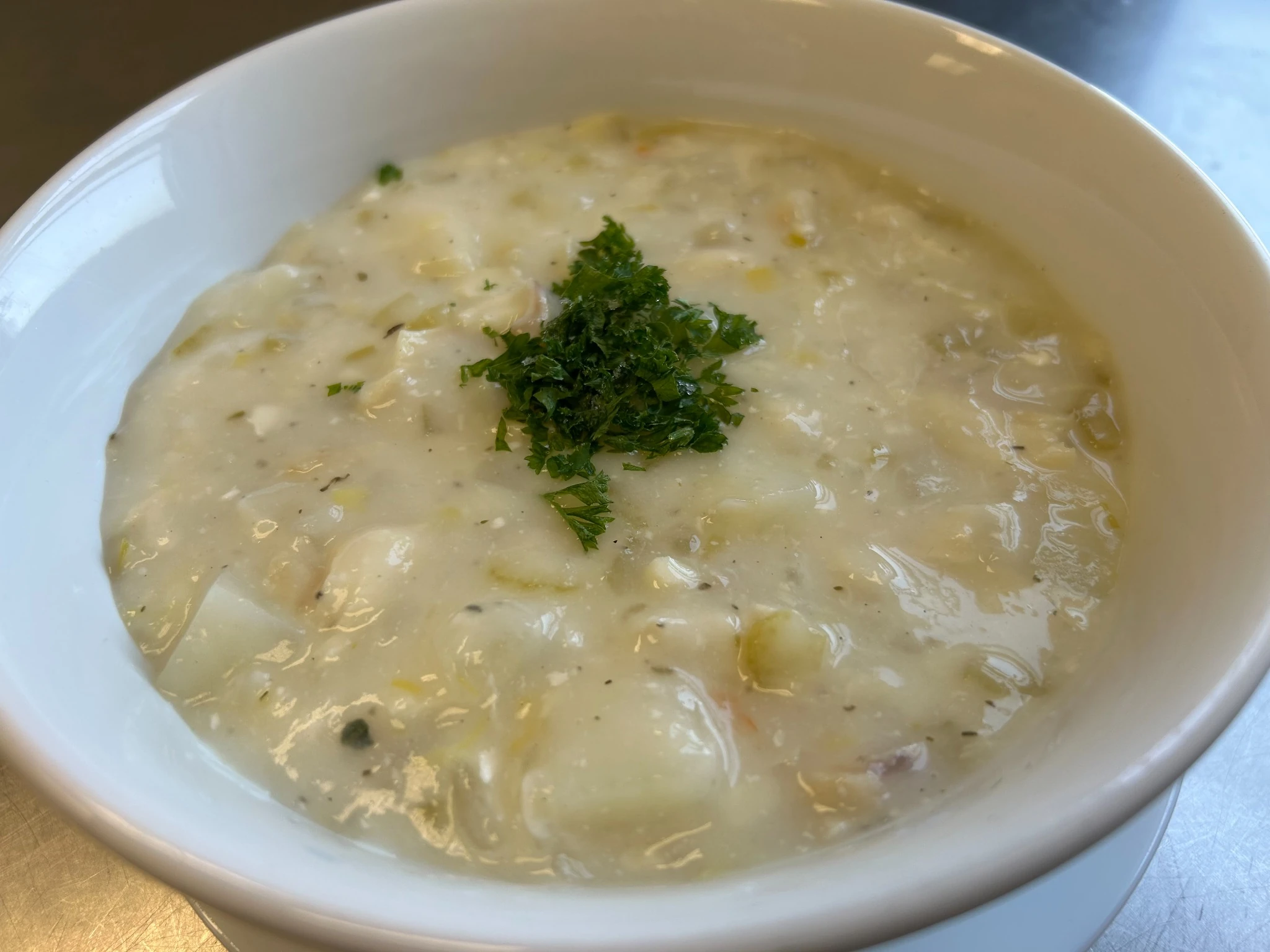 Bowl of fish chowder soup with tender fish, potatoes, herbs, and a parsley garnish in a creamy broth.