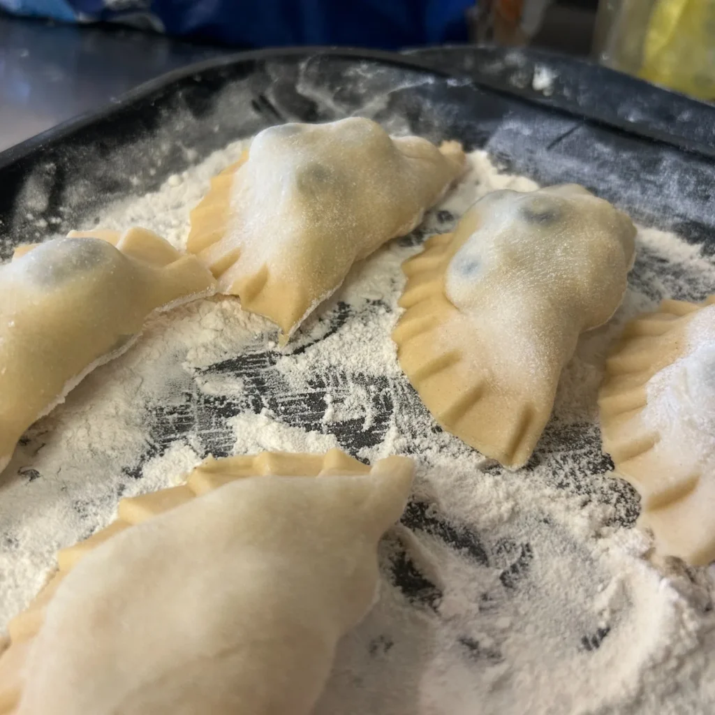 Fresh pierogies resting on a flour-dusted tray, ready to cook.