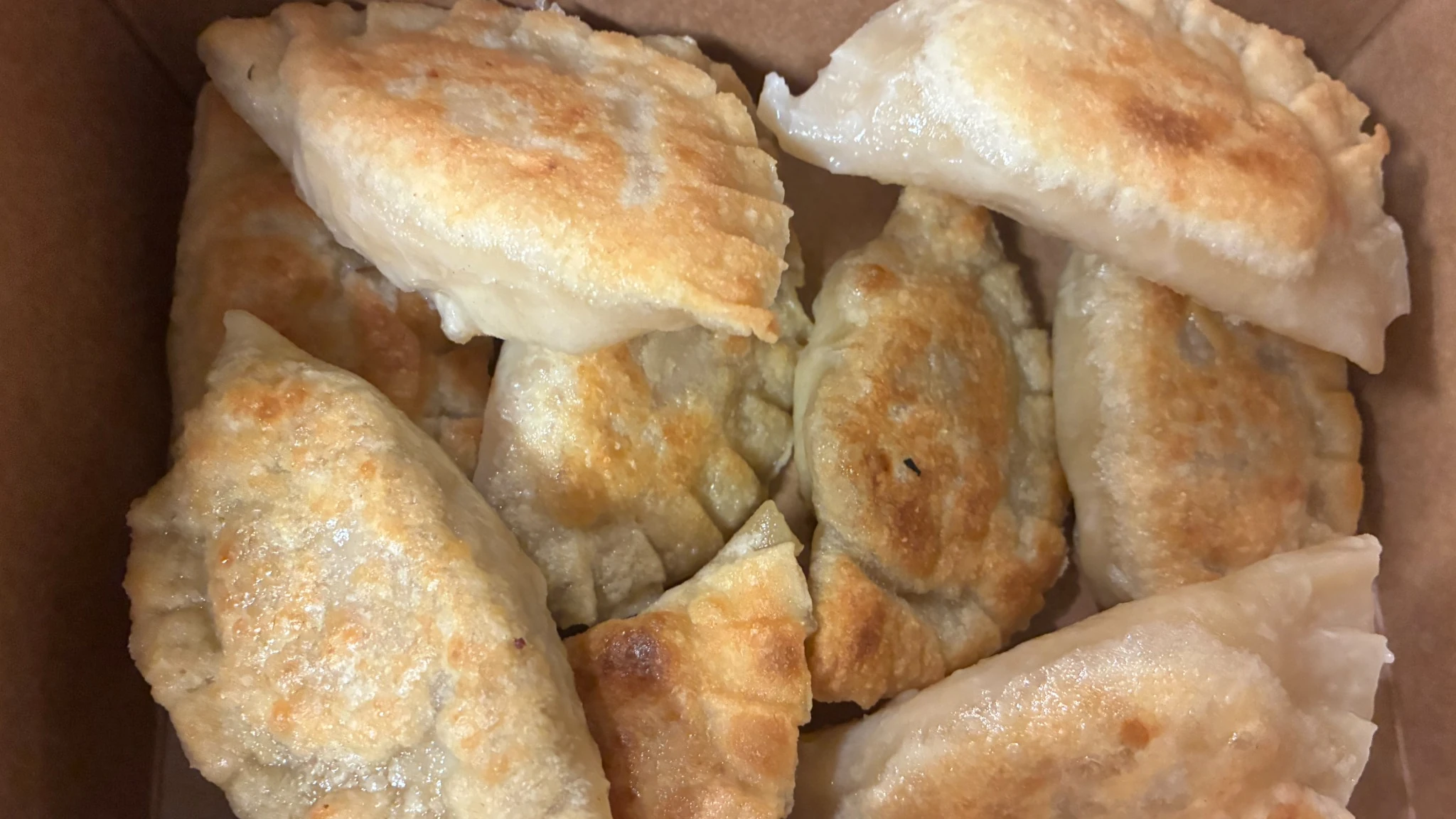 Pan-fried pierogies packed in a brown bio leak-proof takeout box, photographed from above.