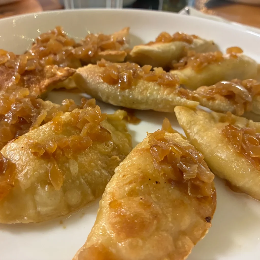 Handmade classic pierogies topped with sautéed onions on a white plate.