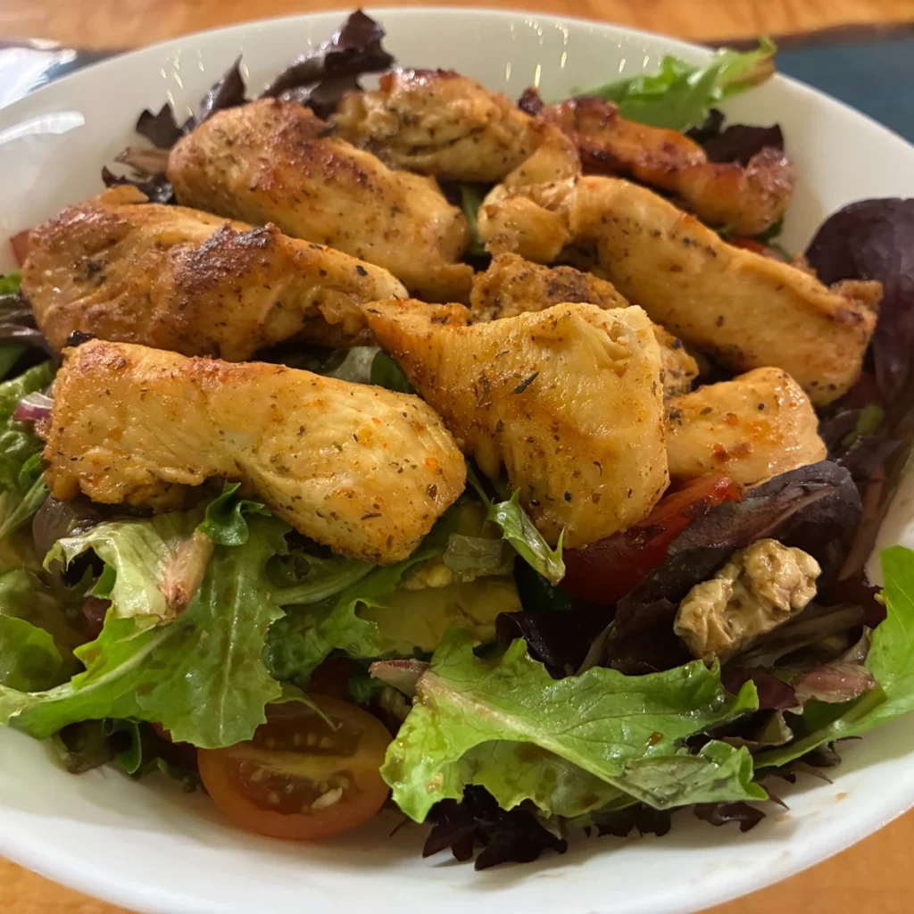Grilled chicken served over a mixed green garden salad with cherry tomatoes in a white bowl.