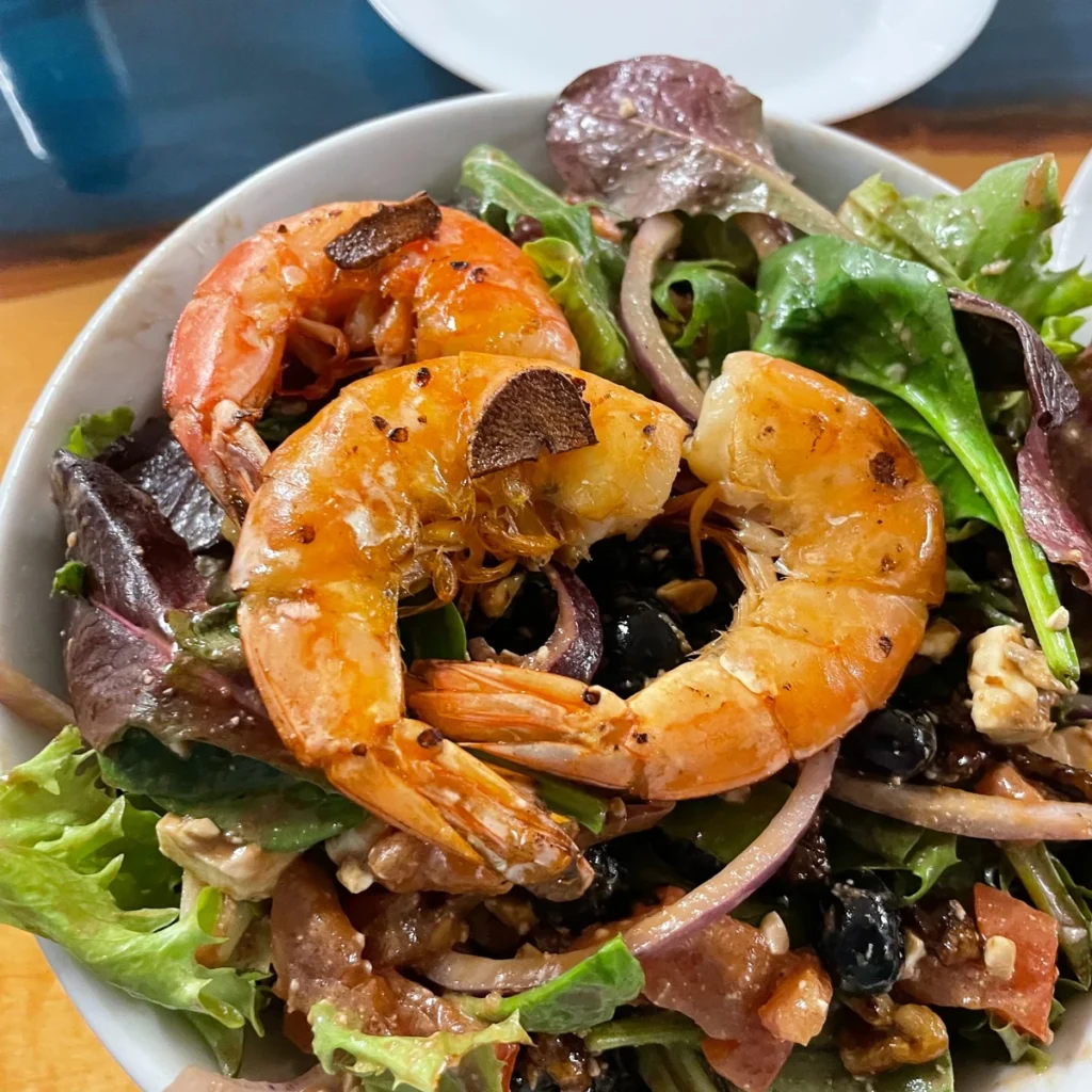 Three jumbo shrimp served over mixed greens with red onion and toppings in a white bowl.