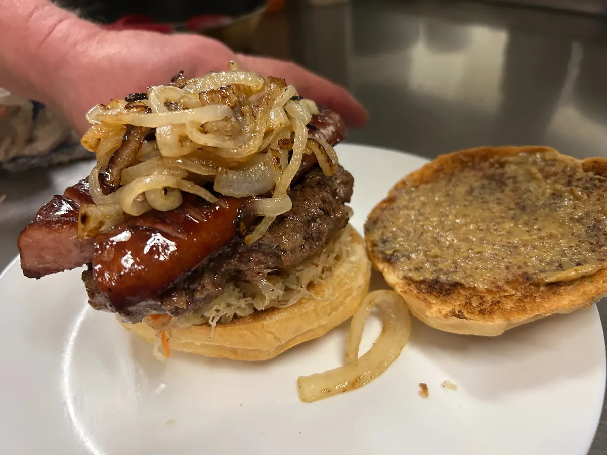 Open-faced kielbasa burger with grilled sausage, sauerkraut and fried onions on a toasted bun during final assembly.