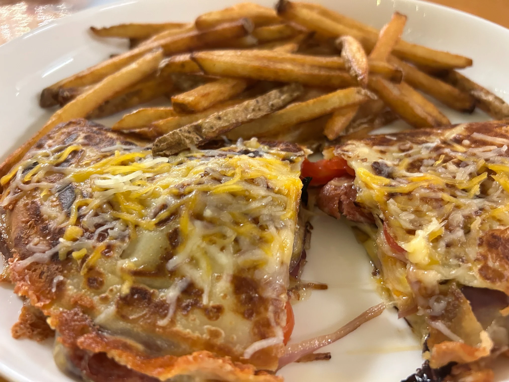 Grilled kielbasa, cheese, and tomato crepe cut into wedges and served with fries on a white plate.
