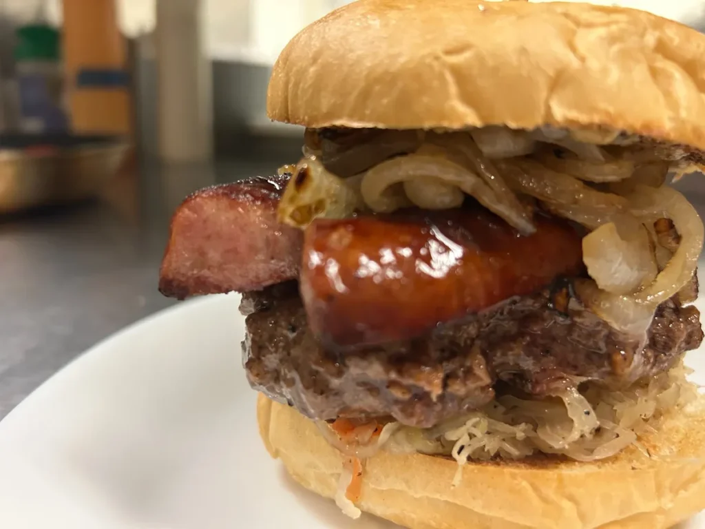 Kielbasa smash burger with grilled sausage, caramelized onions, Slavic mustard, and sauerkraut on a toasted bun.
