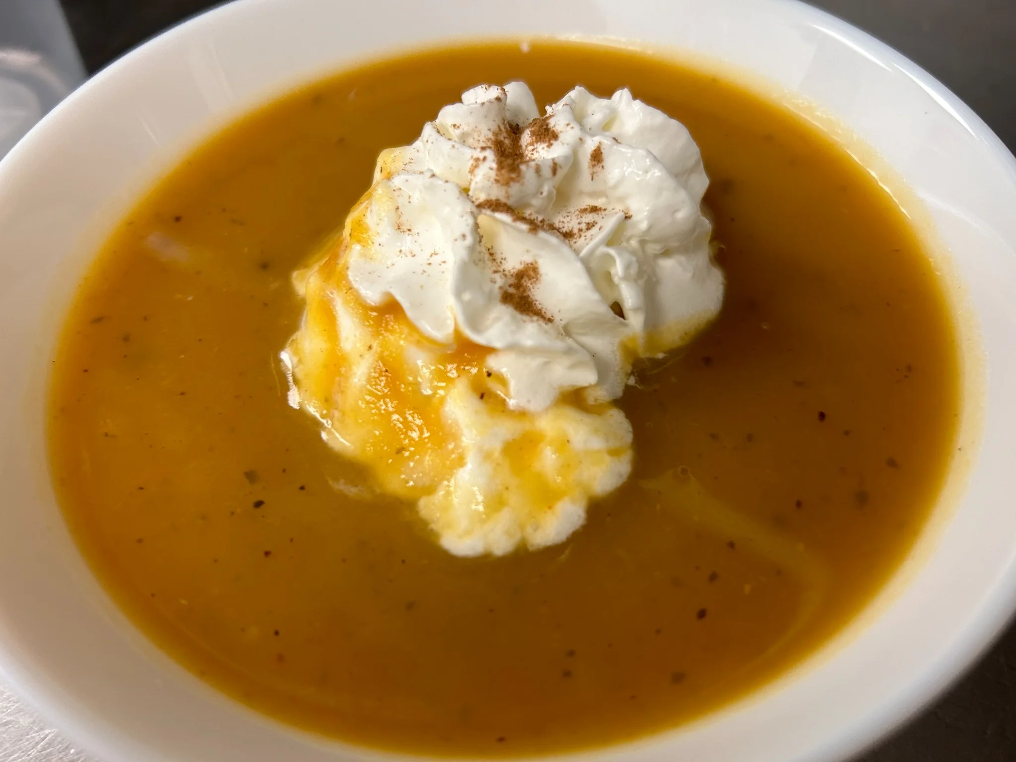 Smooth maple pumpkin soup topped with whipped cream and cinnamon in a white bowl.