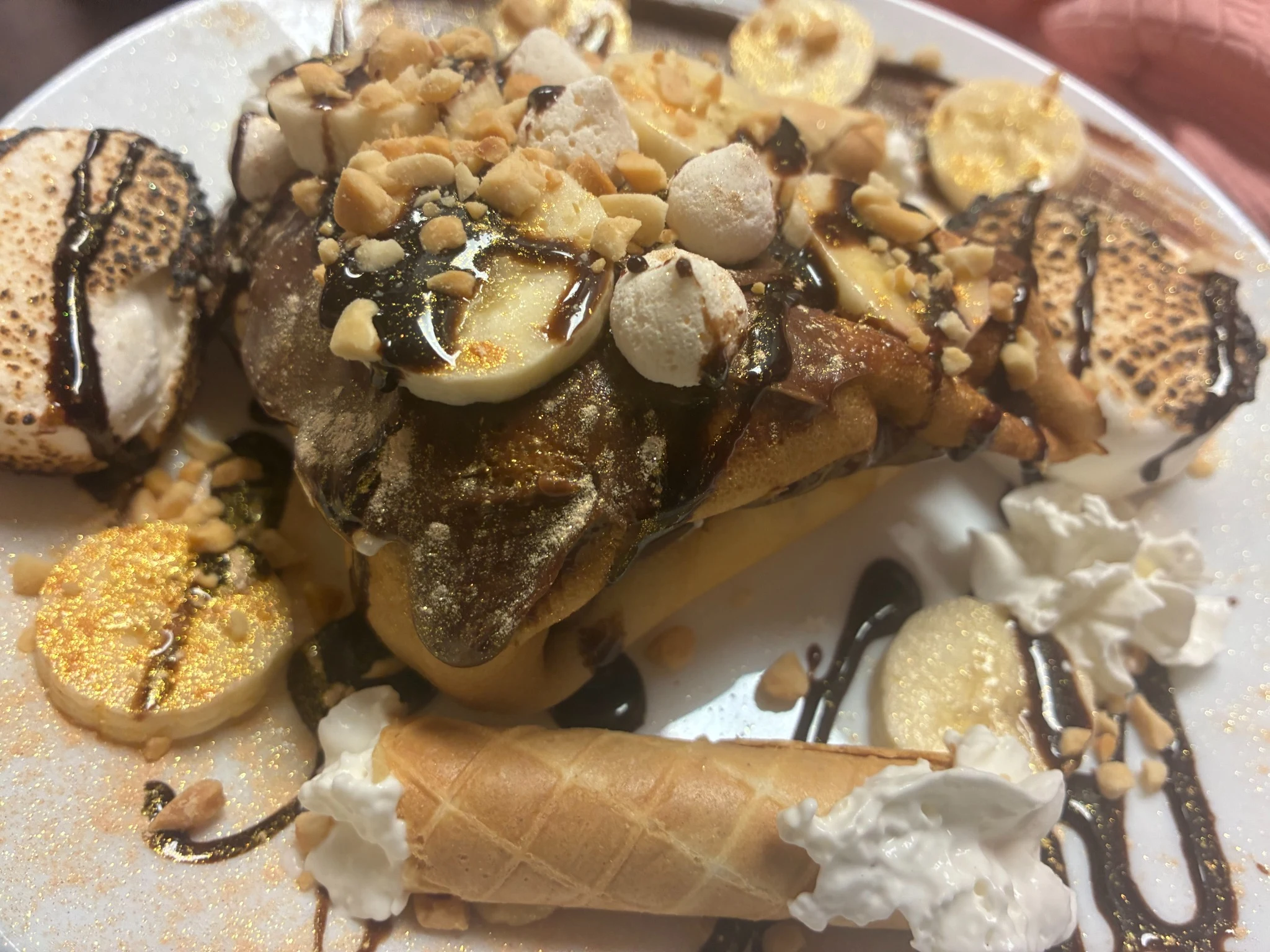 Overloaded Nutella s'mores blintz crepe topped with banana slices, chopped nuts, mini marshmallows, toasted marshmallows, and cream-filled wafer rolls.