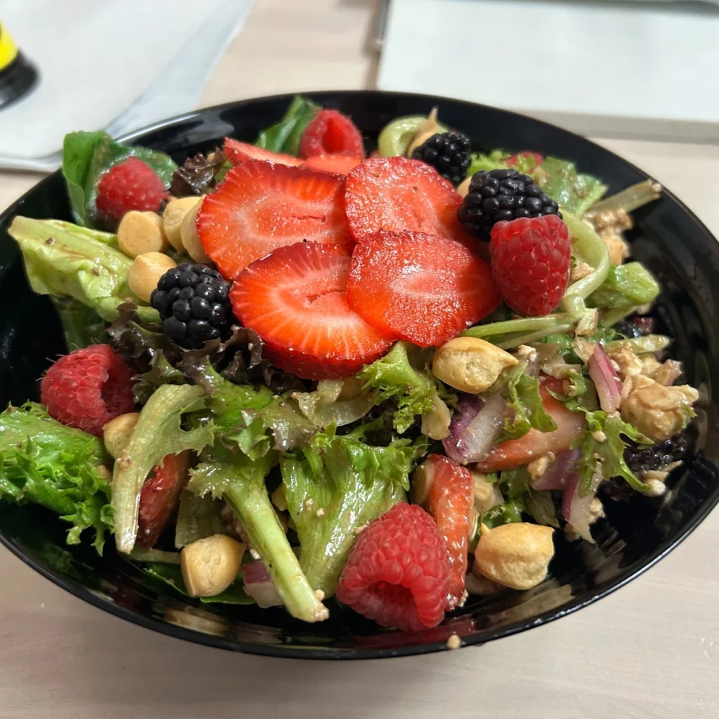 Mixed greens salad with sliced strawberries, raspberries, blackberries, and crunchy nuts in a black bowl.
