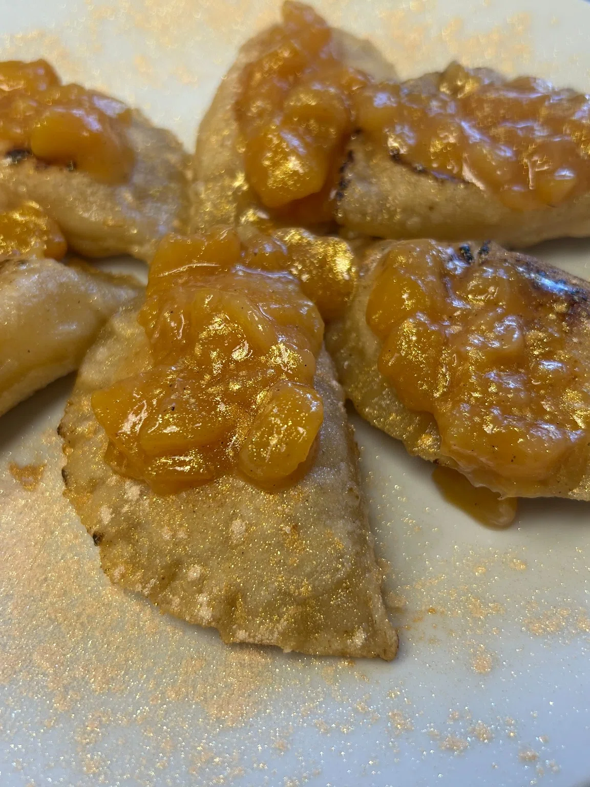 Sweet peach pierogies topped with warm homemade peach compote and a light dusting of powdered sugar.