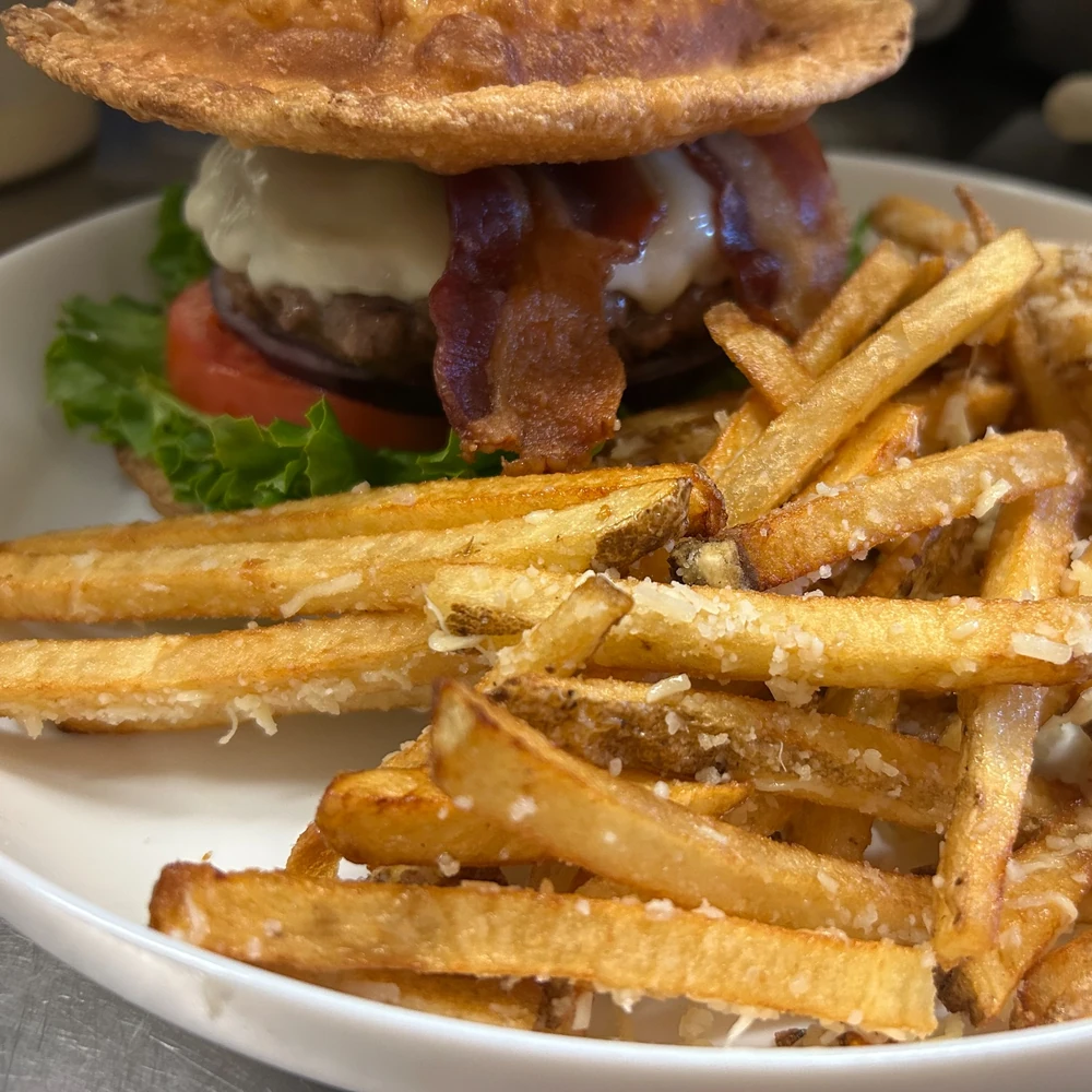 Close-up of a pierogi burger with bacon, melted cheese, and Parmesan fries on a white plate.