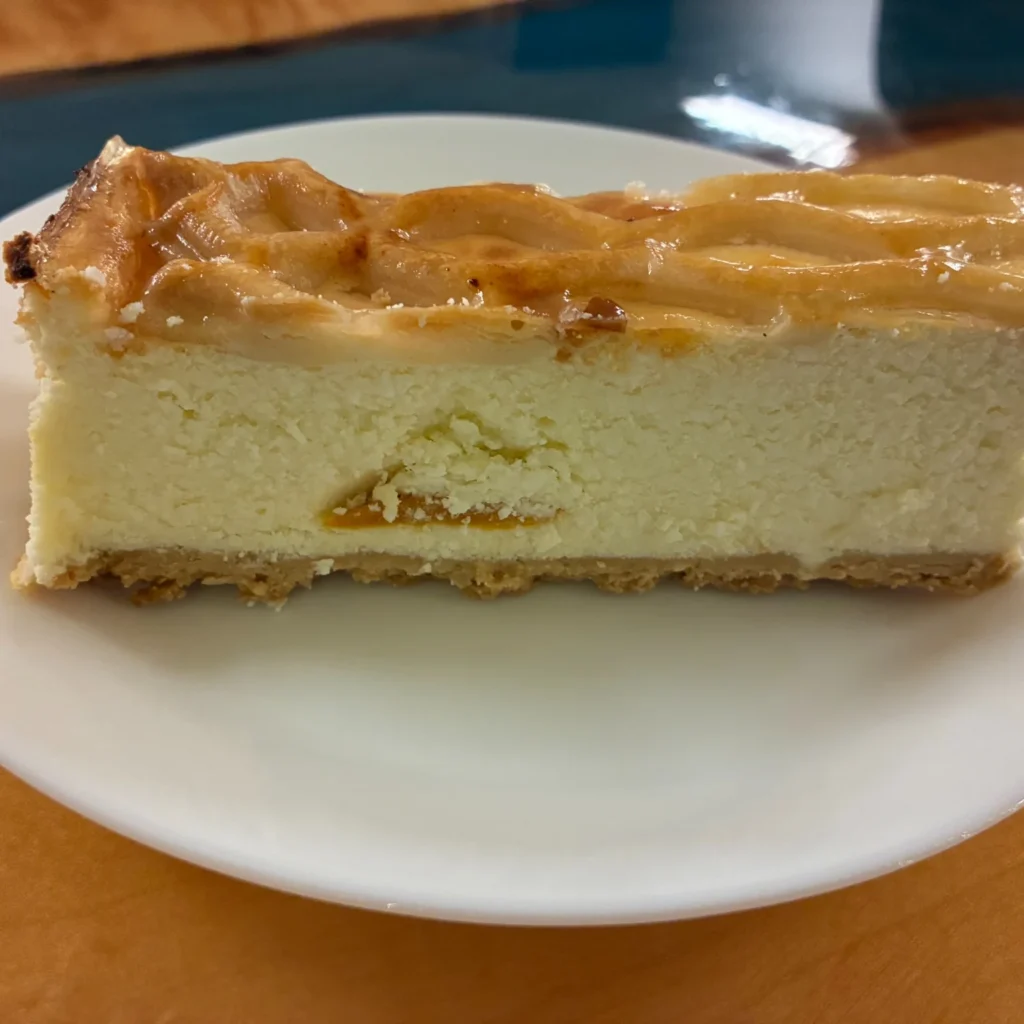 Slice of homemade peach cheesecake with a baked peach layer over thick creamy cheesecake filling.