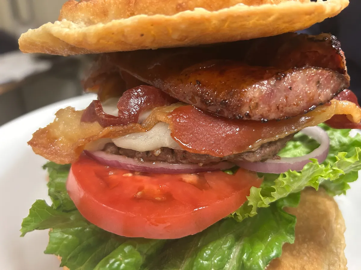 Pierogi smash burger stacked with bacon and kielbasa sausage over lettuce, tomato and red onion.