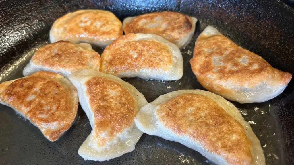 Close-up of pierogies browning in oil in a cast-iron skillet.