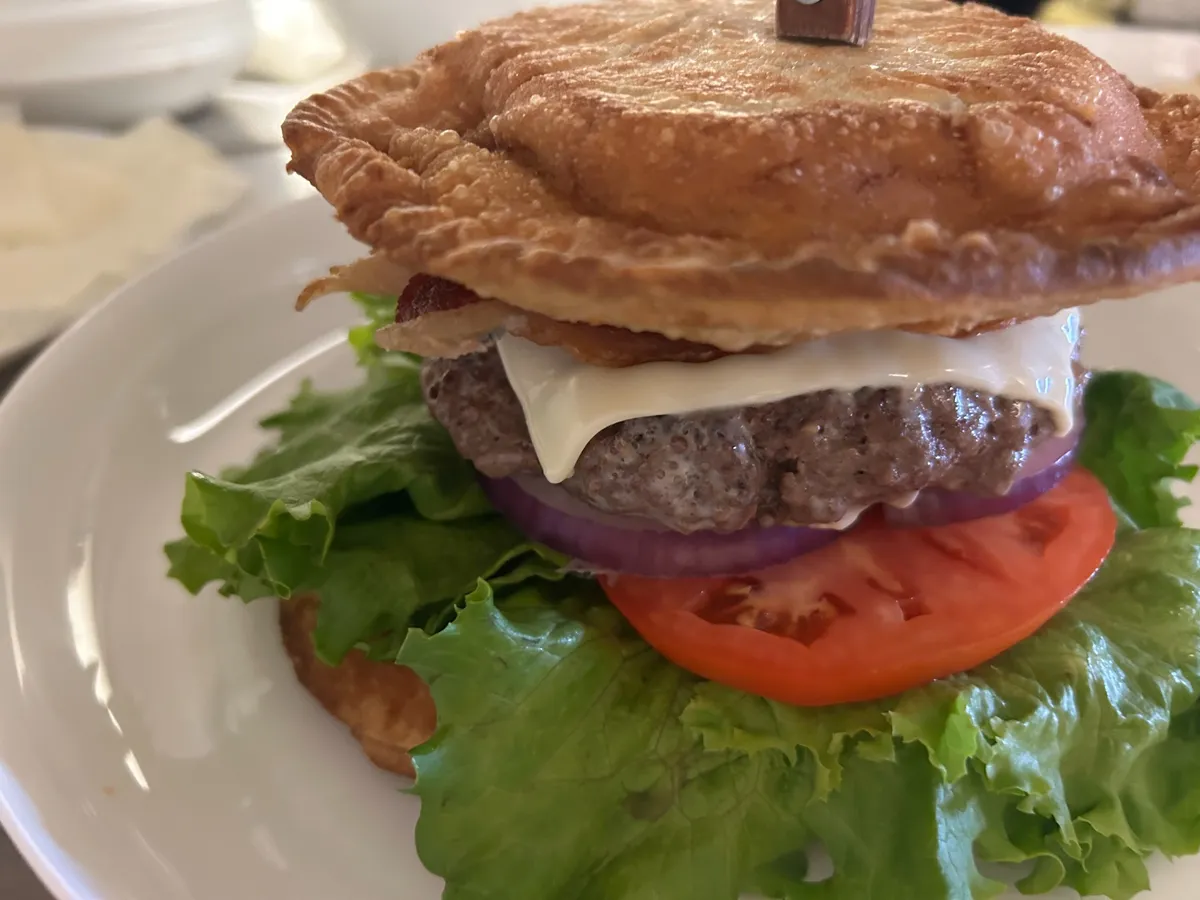 Close-up of a pierogi smash burger with a fried pierogi bun, bacon, cheese, lettuce, tomato and red onion.