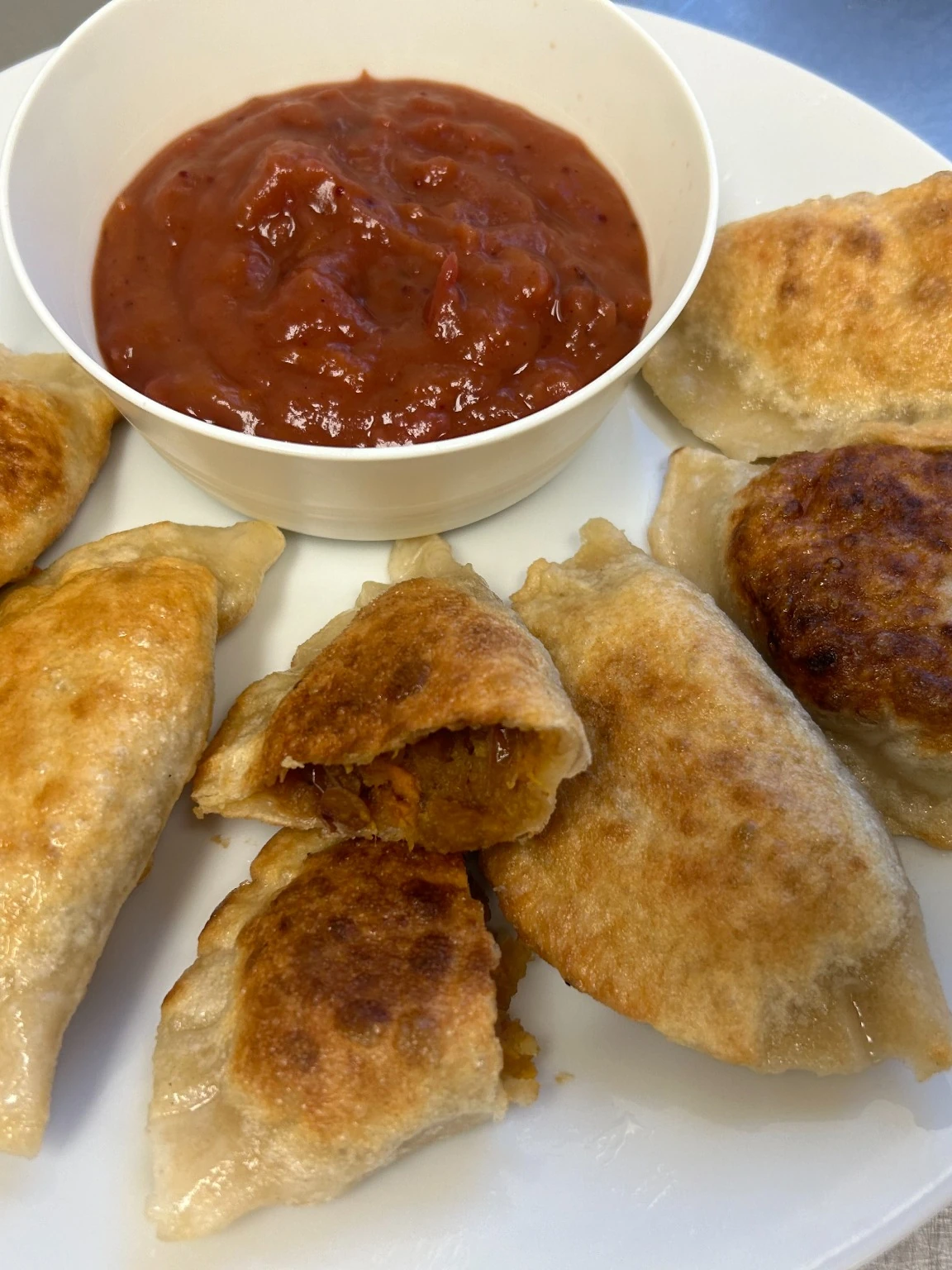 Kat's seasonal Pilgrim's Harvest pierogies with a red homemade cranberry dipping sauce on a white plate.