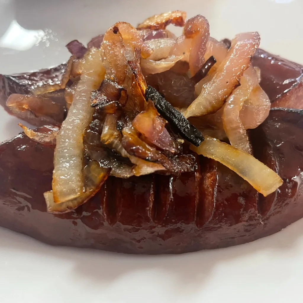 Polish kielbasa sausage topped with caramelized onions on a white plate.