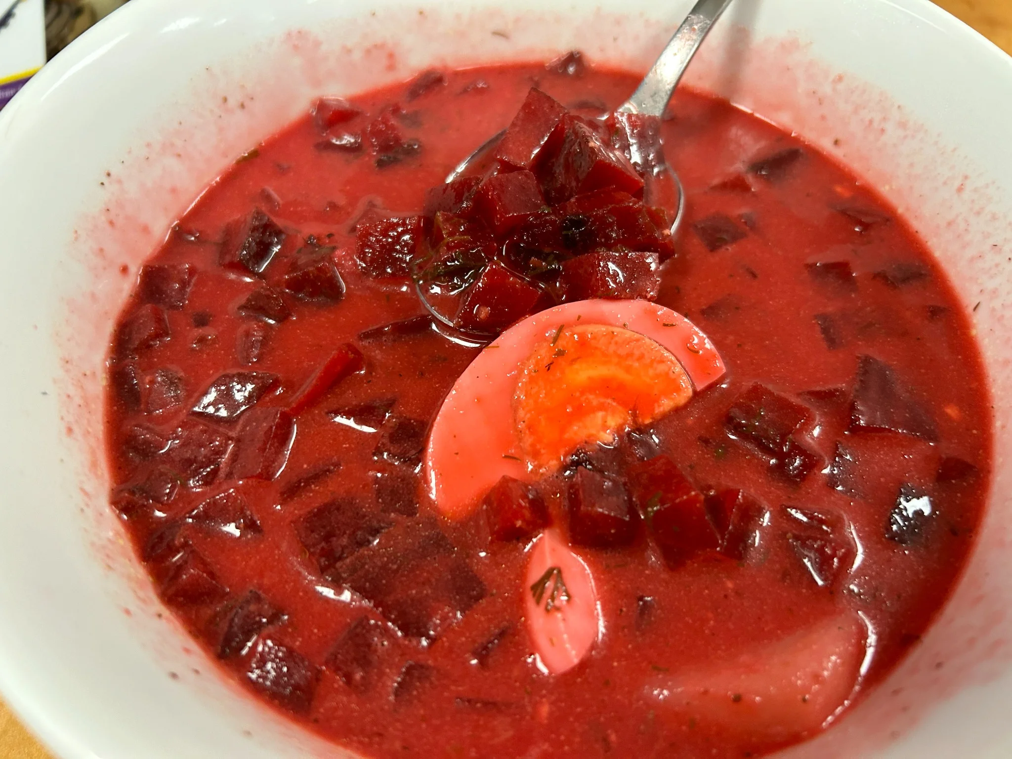 Bright red beet borscht Slavic soup with chopped beets and a halved egg in a white bowl.