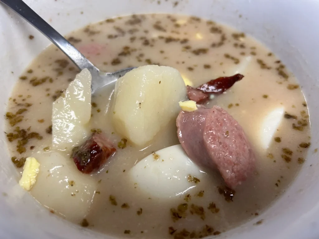 Bowl of Polish Żurek sour rye soup with white kielbasa sausage, potatoes, egg, and marjoram in a creamy broth.