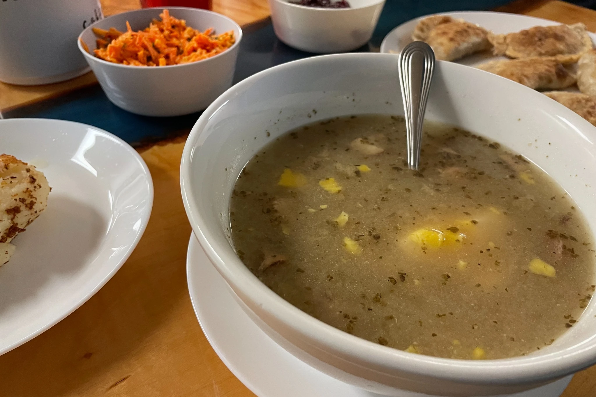 Bowl of Kat’s Polish żurek soup served with pierogies, carrot salad, and side dishes on a dining table.