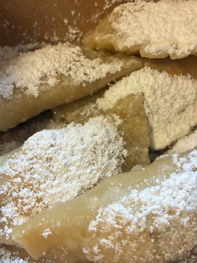 Fresh prune pierogies dusted with powdered sugar in a gourmet takeout box.