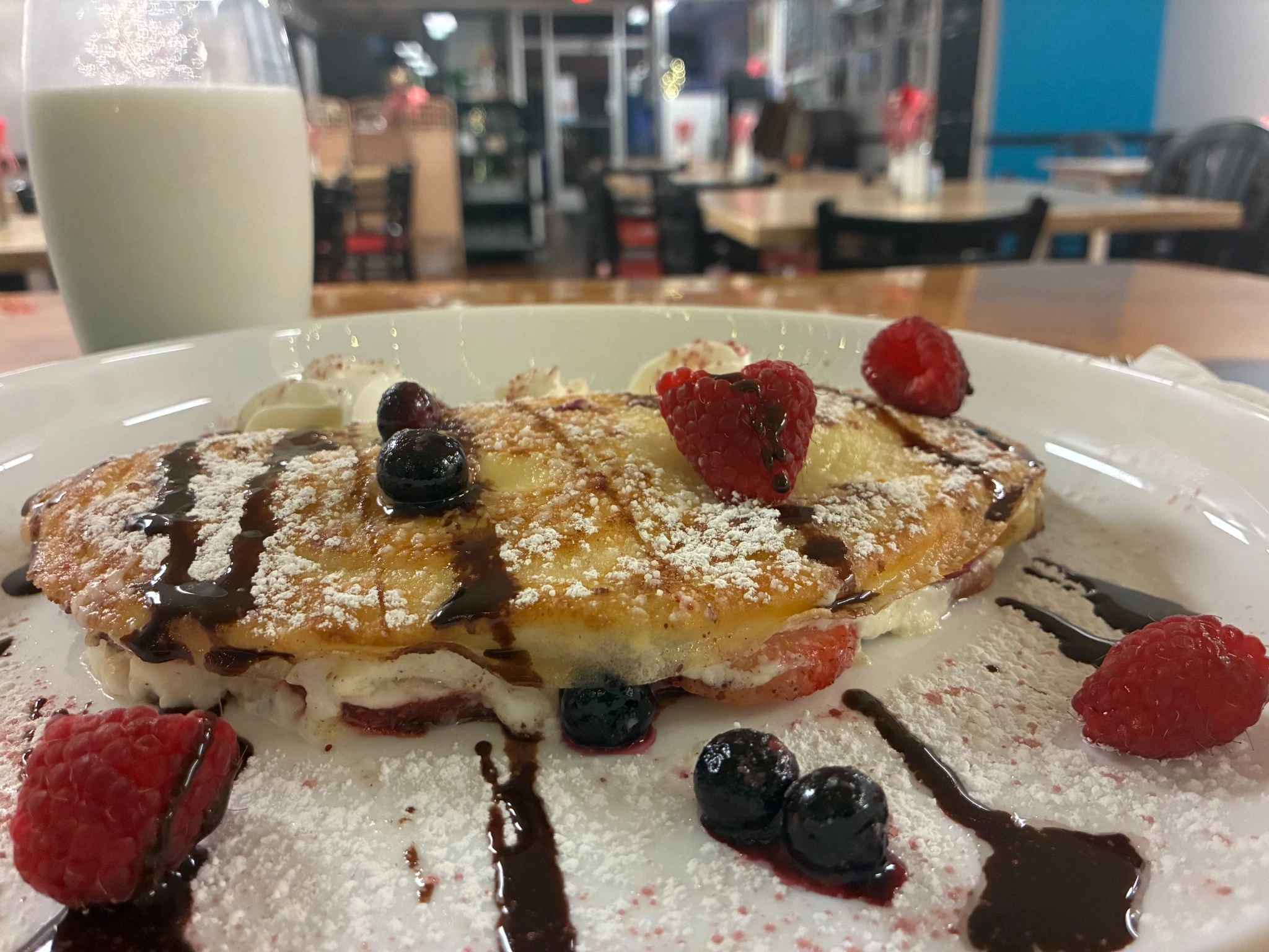 Raspberry and blueberry sweet cheese crepe topped with powdered sugar, chocolate drizzle, and fresh berries.