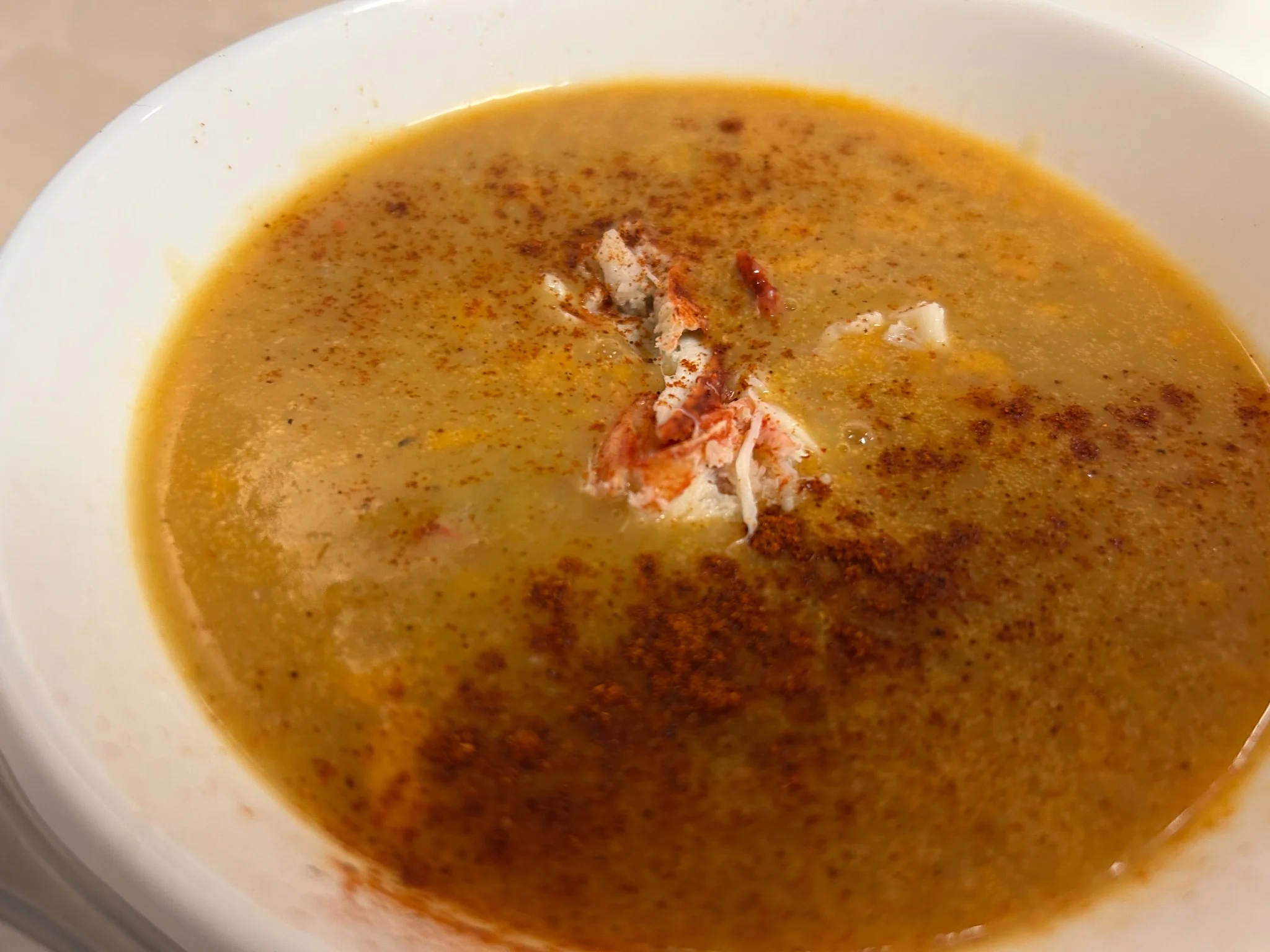 Creamy lobster bisque topped with pieces of lobster and paprika in a white bowl.