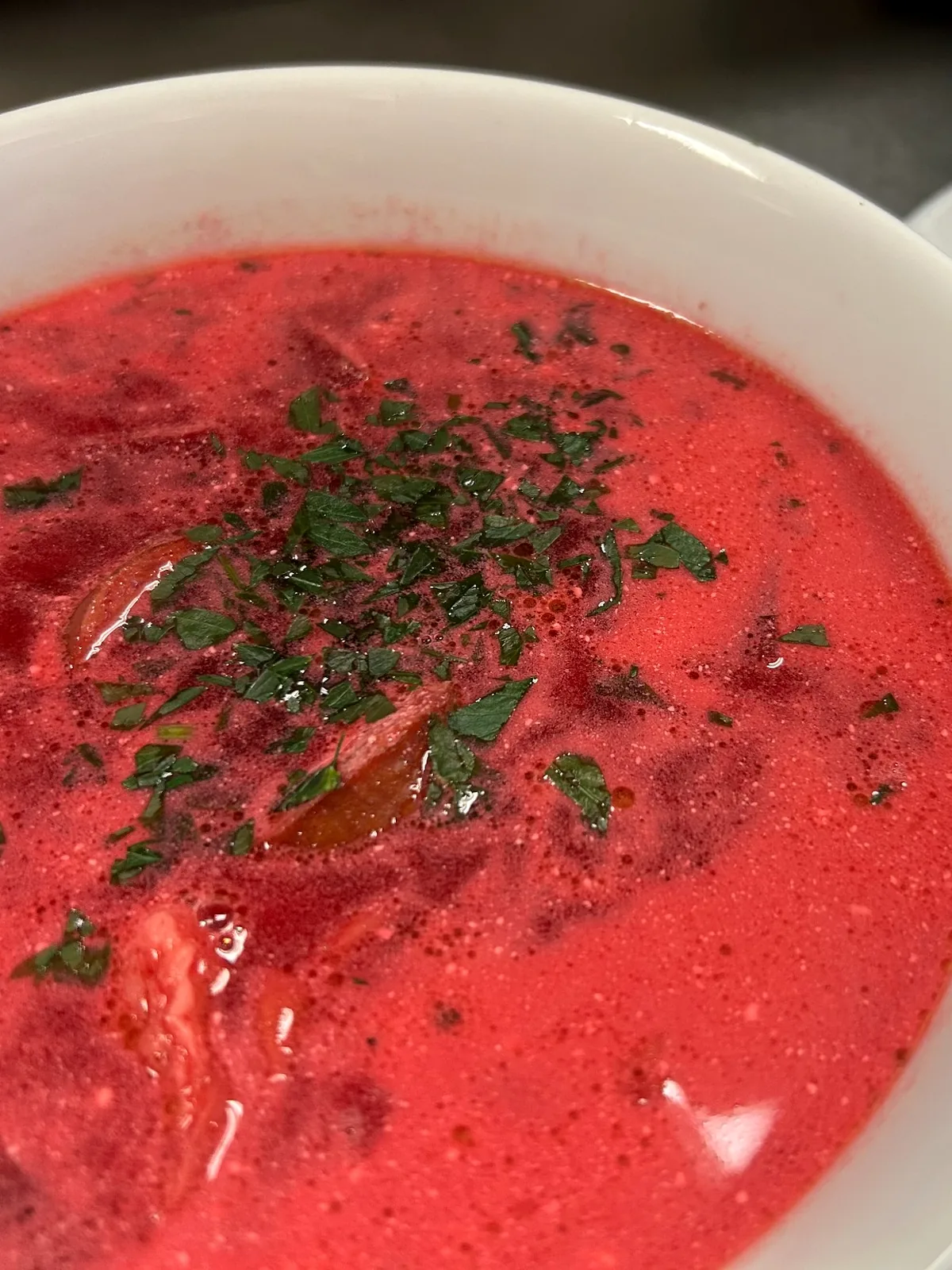 Bowl of red beet borscht soup topped with fresh herbs.