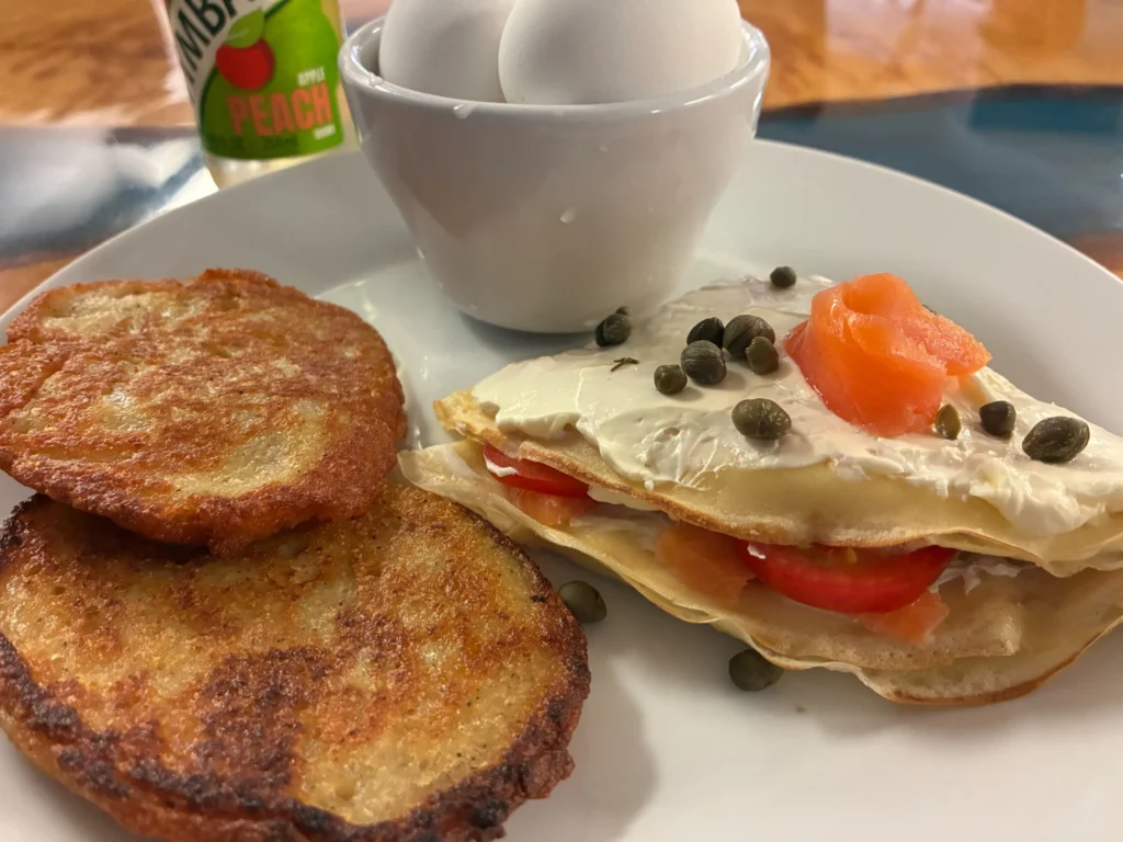 Salmon and cream cheese lox blintz having tomatoes and capers served with potato pancake blinis and hard-boiled eggs.