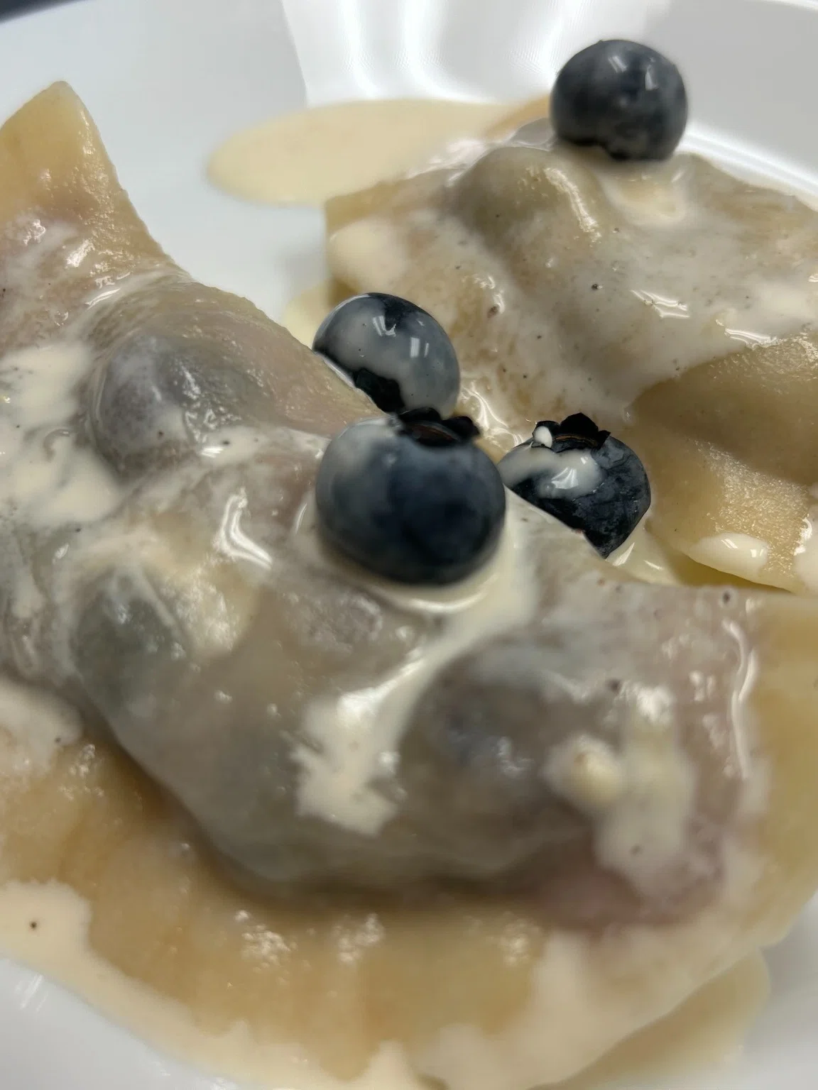 Blueberry pierogi topped with cream sauce and fresh blueberries on a white plate.
