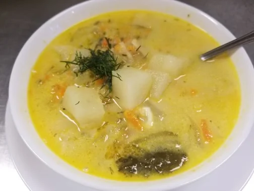 Creamy shredded pickle soup with potatoes, carrots, herbs, and dill in a white bowl.