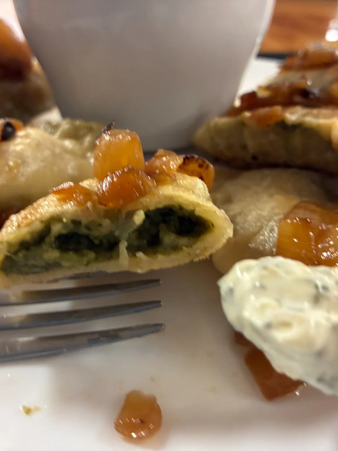 Spinach and feta pierogi cut open to show the green spinach-feta filling, served with sautéed onions and a creamy artichoke dip.