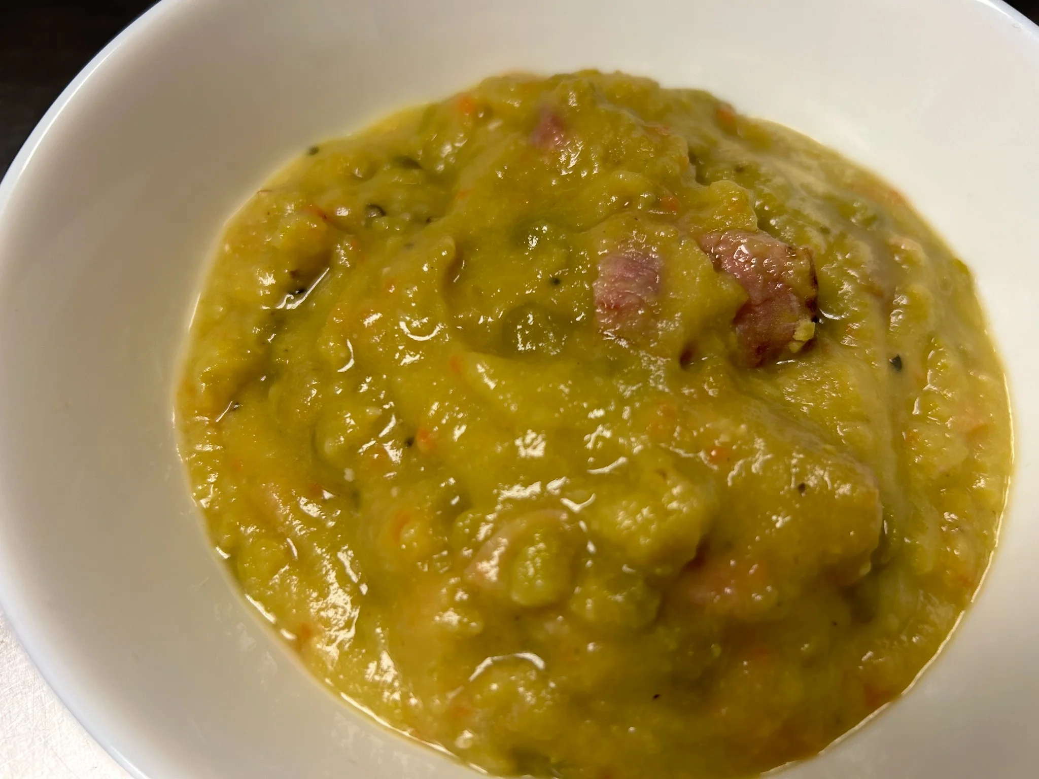 Thick split pea and ham soup with pieces of ham in a white bowl.