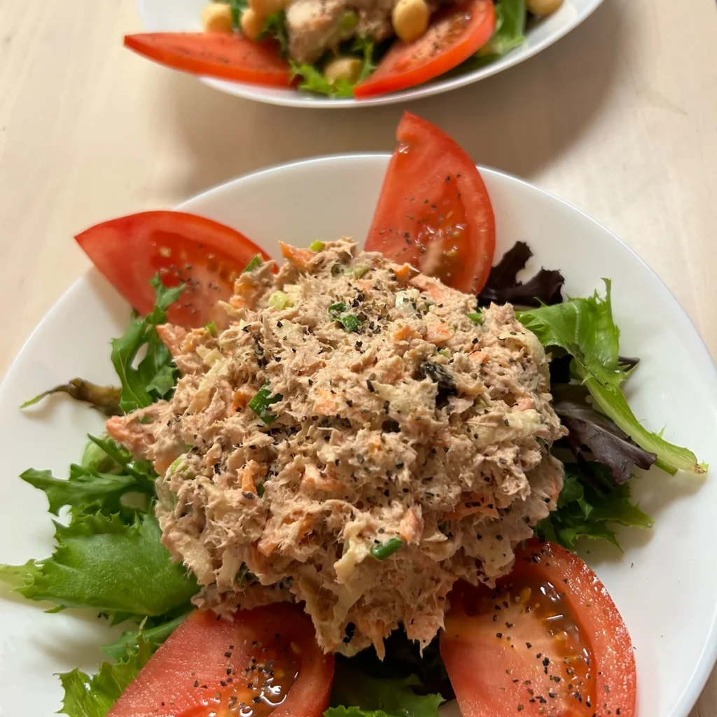 Two plated tuna salads served over mixed greens with tomato wedges.