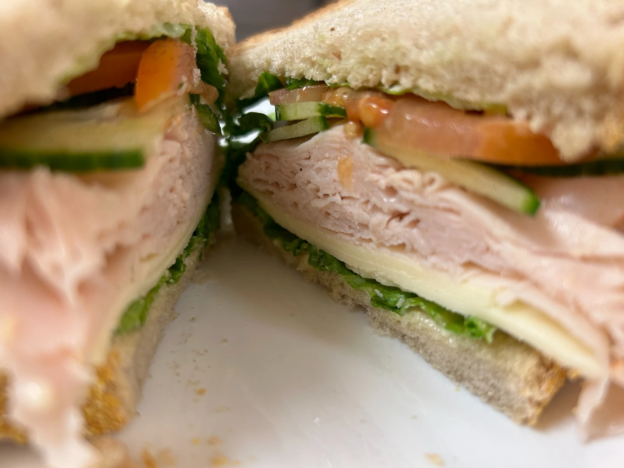 Turkey sandwich halves on rye bread with sliced turkey, cheese, lettuce, tomato, and cucumber.