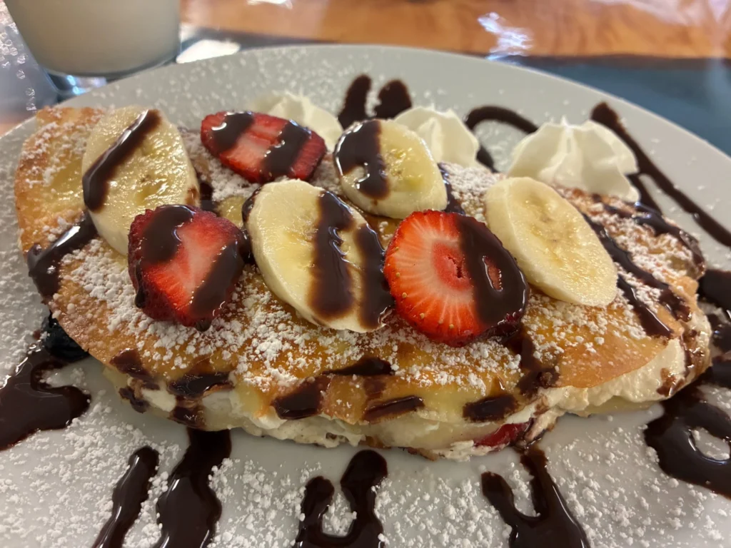Strawberry banana sweet cheese crepe topped with powdered sugar, chocolate drizzle, sliced bananas, strawberries, and whipped cream.