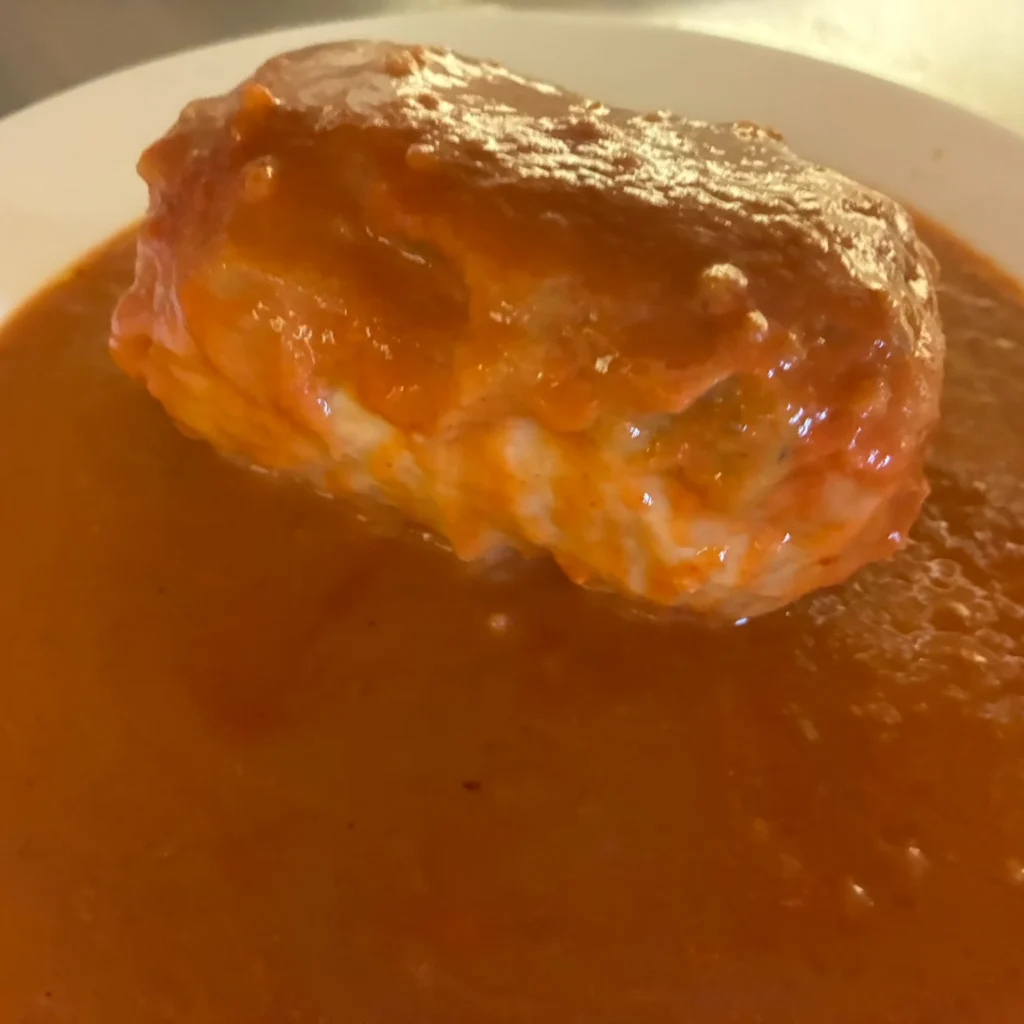 XL halupki stuffed cabbage roll served in tomato sauce on a white plate.