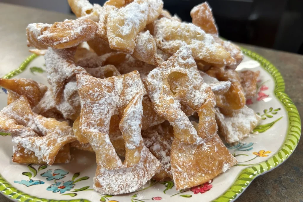 Traditional angel bow tie chruściki dusted generously with powdered sugar on a floral plate.