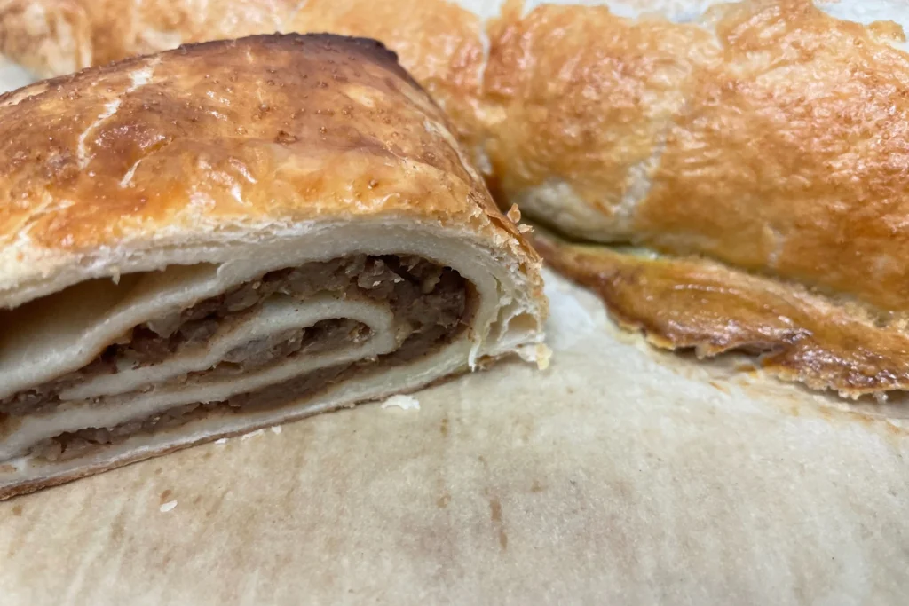 Close-up of Kat’s apple strudel showing tender apple filling in rolled pastry, with a full baked strudel in the background.