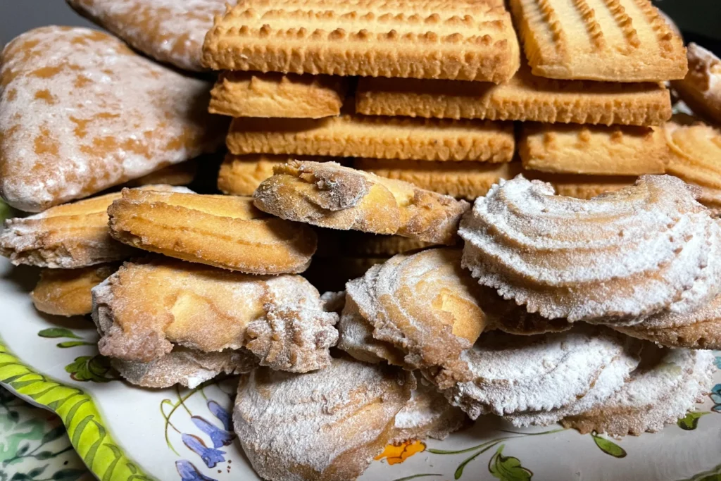 Assorted tea cookies, butter biscuits, and powdered sugar pastries stacked in a generous pile on a floral platter.