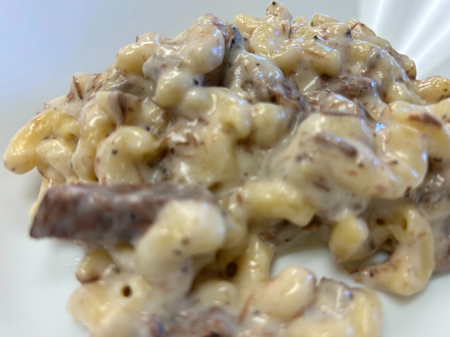 Creamy brisket mac and cheese in a white bowl with tender pieces of brisket and rich cheese sauce.