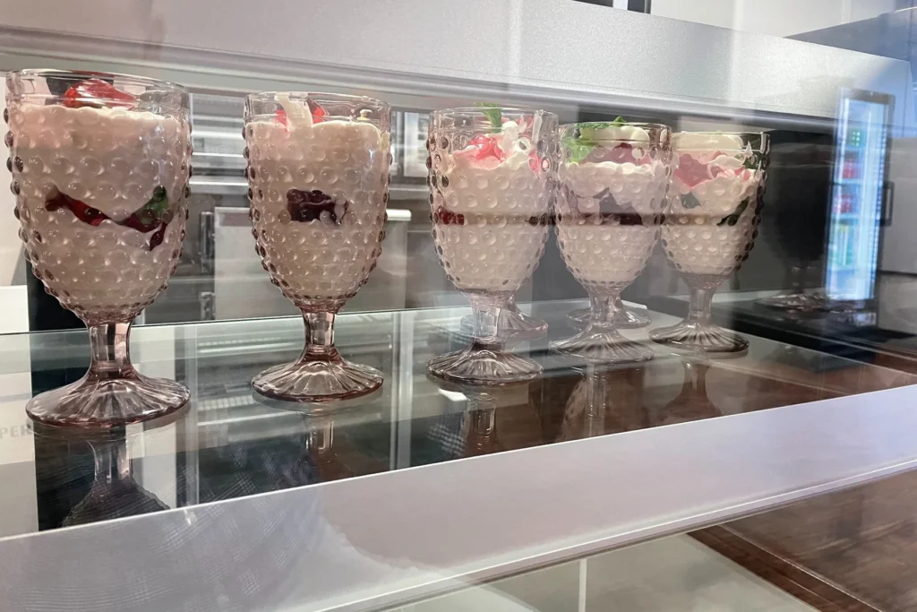 Glass dessert cups layered with cream, fruit, and garnish lined up in a refrigerated display.