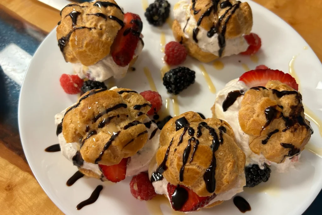 Berry cream puff pastries filled with real cream and strawberries, finished with chocolate drizzle and fresh berries.